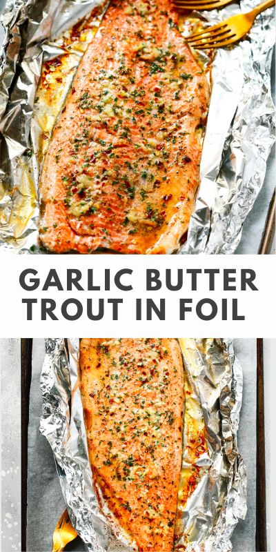 Baked trout in foil, drizzled with garlic butter, with a golden crust and herbs, served on a wooden board, with a slice of lemon and fresh herbs nearby.